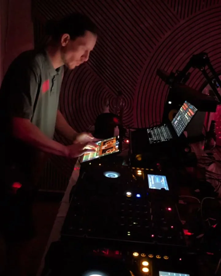 Interaktiv Tap on an iPad in a club booth, both hands on the surface, with Traktor running on the laptop beside it.